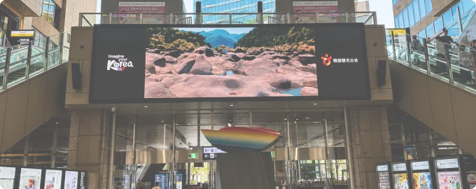 Digital out-of-home screen above a busy station entrance in Japan